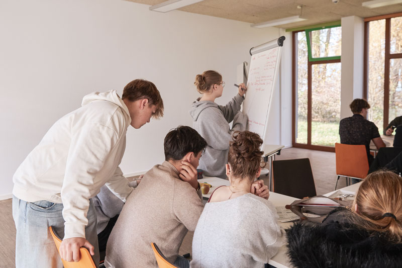 Mehrere Jugendliche arbeiten gemeinsam an einem Flipchart und diskutieren in einer Gruppenarbeit.