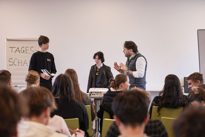 Drei Personen stehen vor einer Gruppe Jugendlicher und präsentieren Inhalte auf einem Flipchart.
