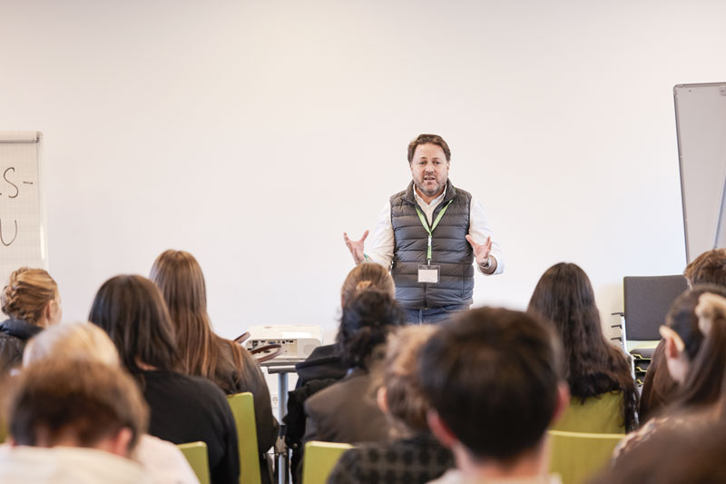 Daniel Harrich steht vor einer sitzenden Gruppe junger Menschen und hält einen Vortrag.