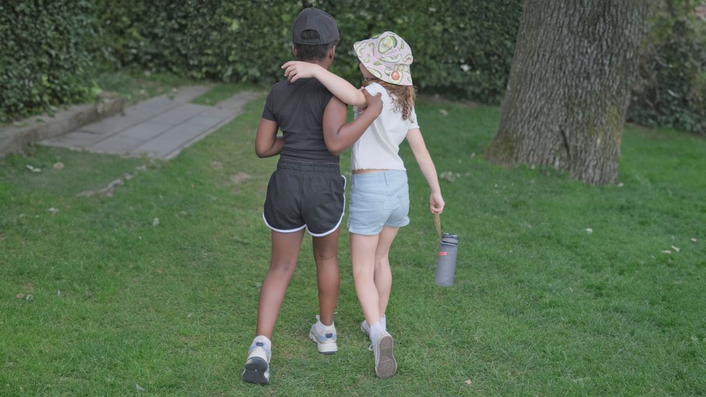 Zwei Mädchen gehen zusammen über eine Wiese.