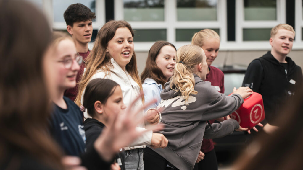 Eine Gruppe junger Klimascouts nimmt vor einem Gebäude an einem Bewegungsspiel mit einem großen roten Würfel teil.