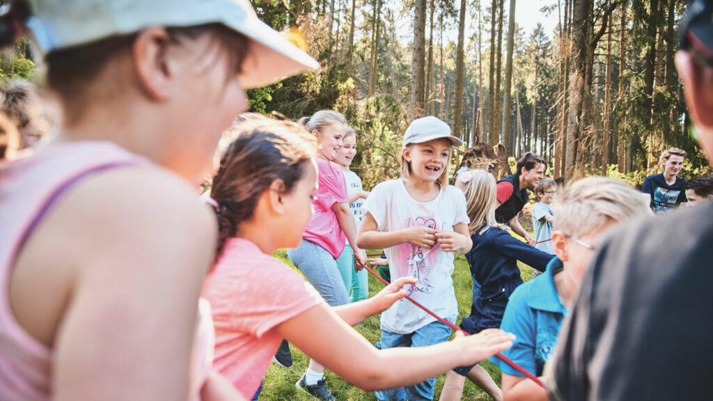 Eine Gruppe junger Klimascouts nimmt auf einer Waldlichtung gemeinsam an einem Bewegungsspiel mit einem roten Seil teil.