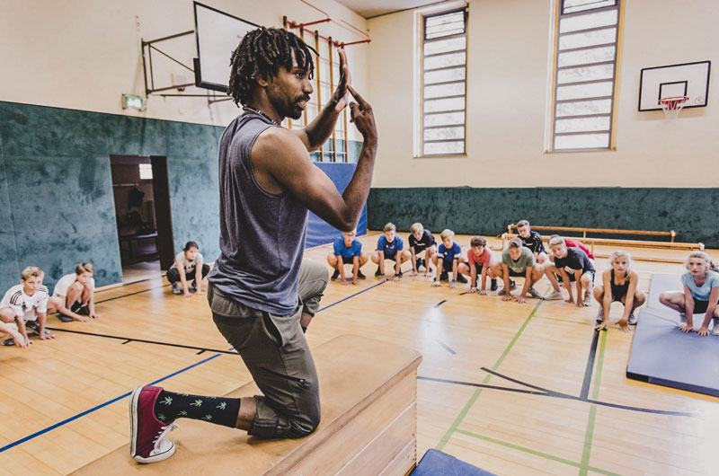 Ein Sportlehrer zeigt seinen Schüler*innen wie eine Übung geht. 