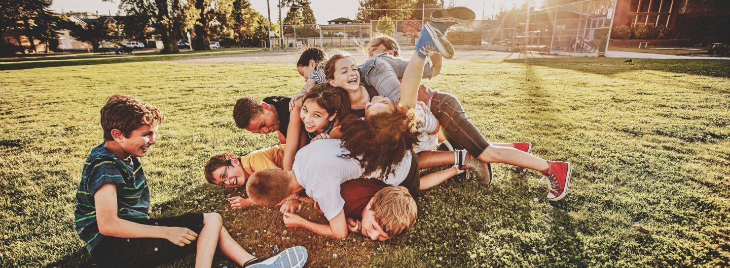 Eine Gruppe von Kindern liegt aufeinander auf einem Fussballplatz.