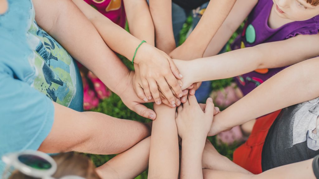 Einige Kinder halten ihre Hände zusammen. In einer Gruppe fällt es leicht Zivilcourage zu fördern.
