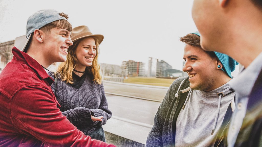 Vier Jugendliche stehen in Berlin und lächeln. Durch ihre Gemeinschaft können sie als Gruppe sicherer auftreten. 